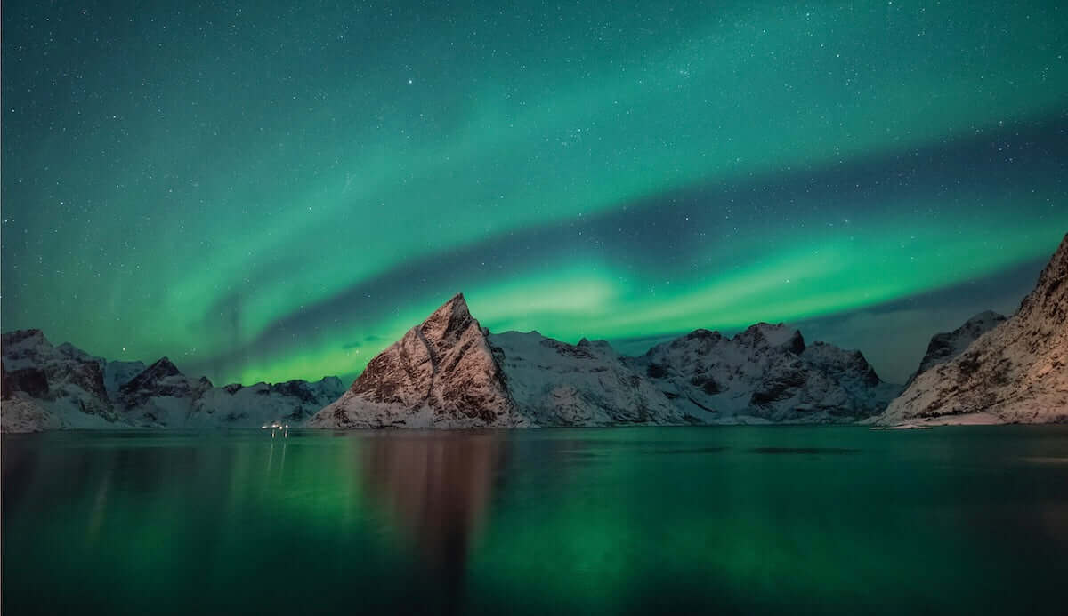 Stunning view of northern lights over snow-capped mountains reflecting in still water under a starry sky.