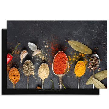 Spice Essence – Inductie Beschermer met lepels vol kruiden en specerijen op een donkere achtergrond.