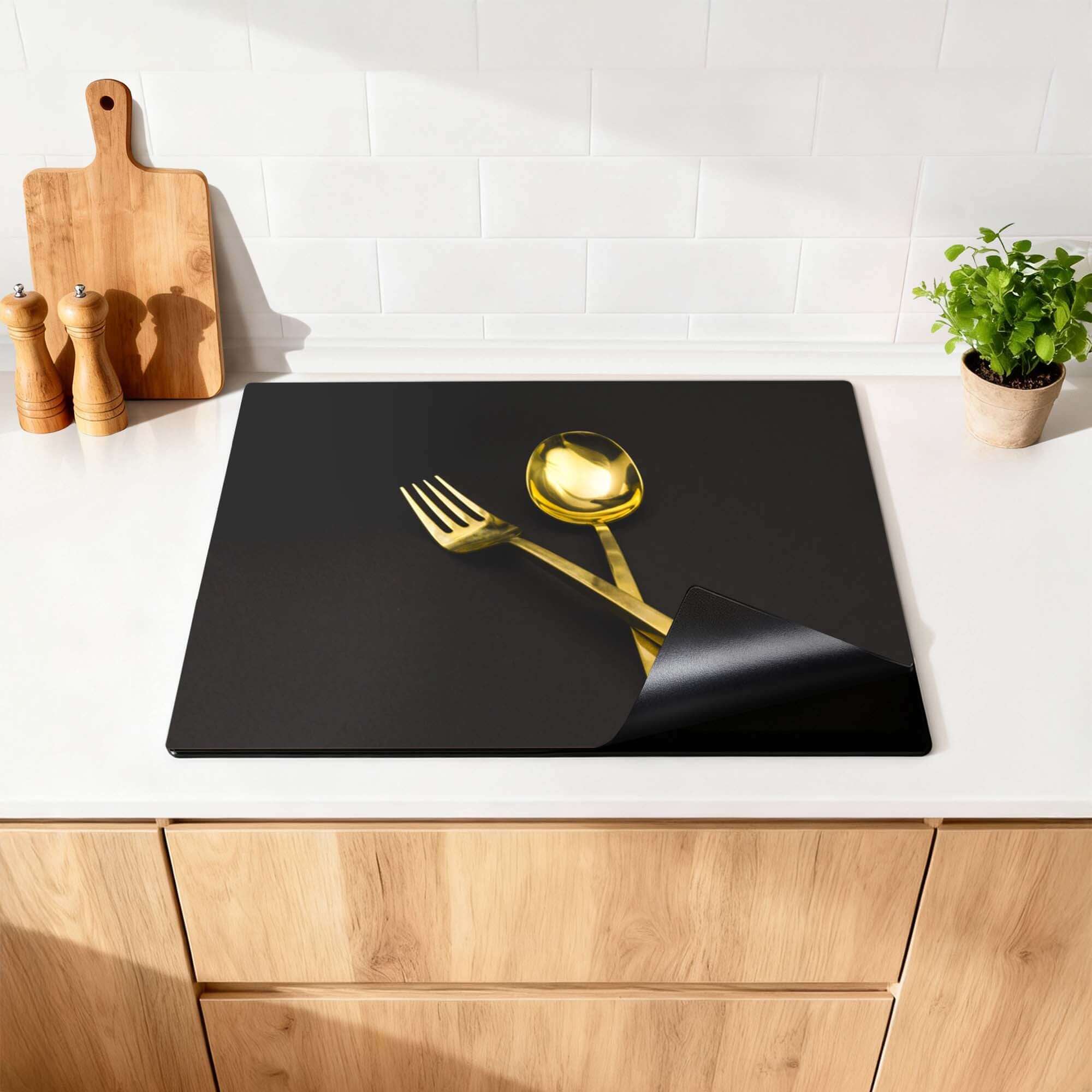 Dining Deluxe - Inductie Beschermer met gouden vork en lepel op zwarte achtergrond.