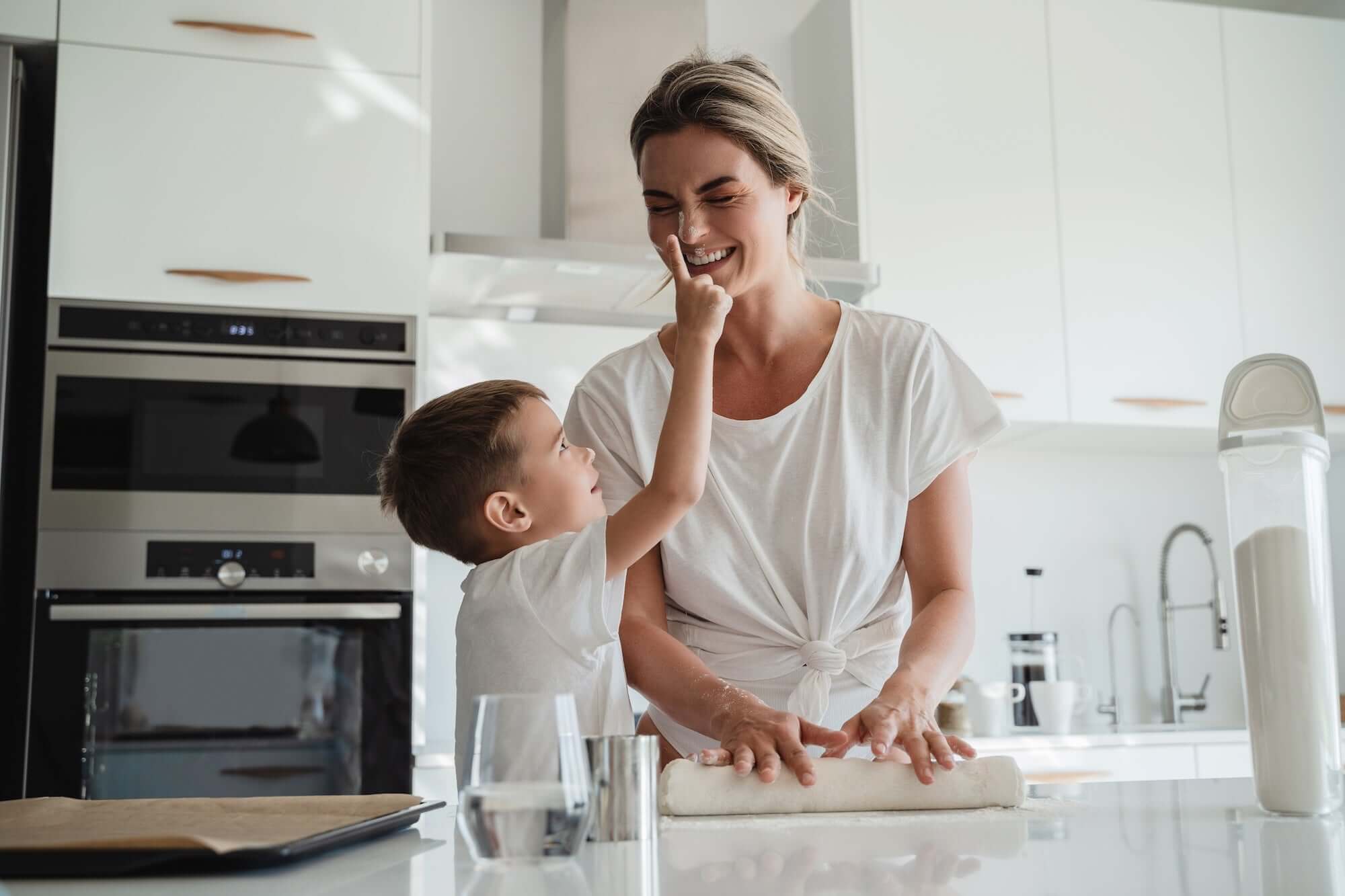 Moeder met zoon in een witte moderne keuken, samen aan het deegrollen.