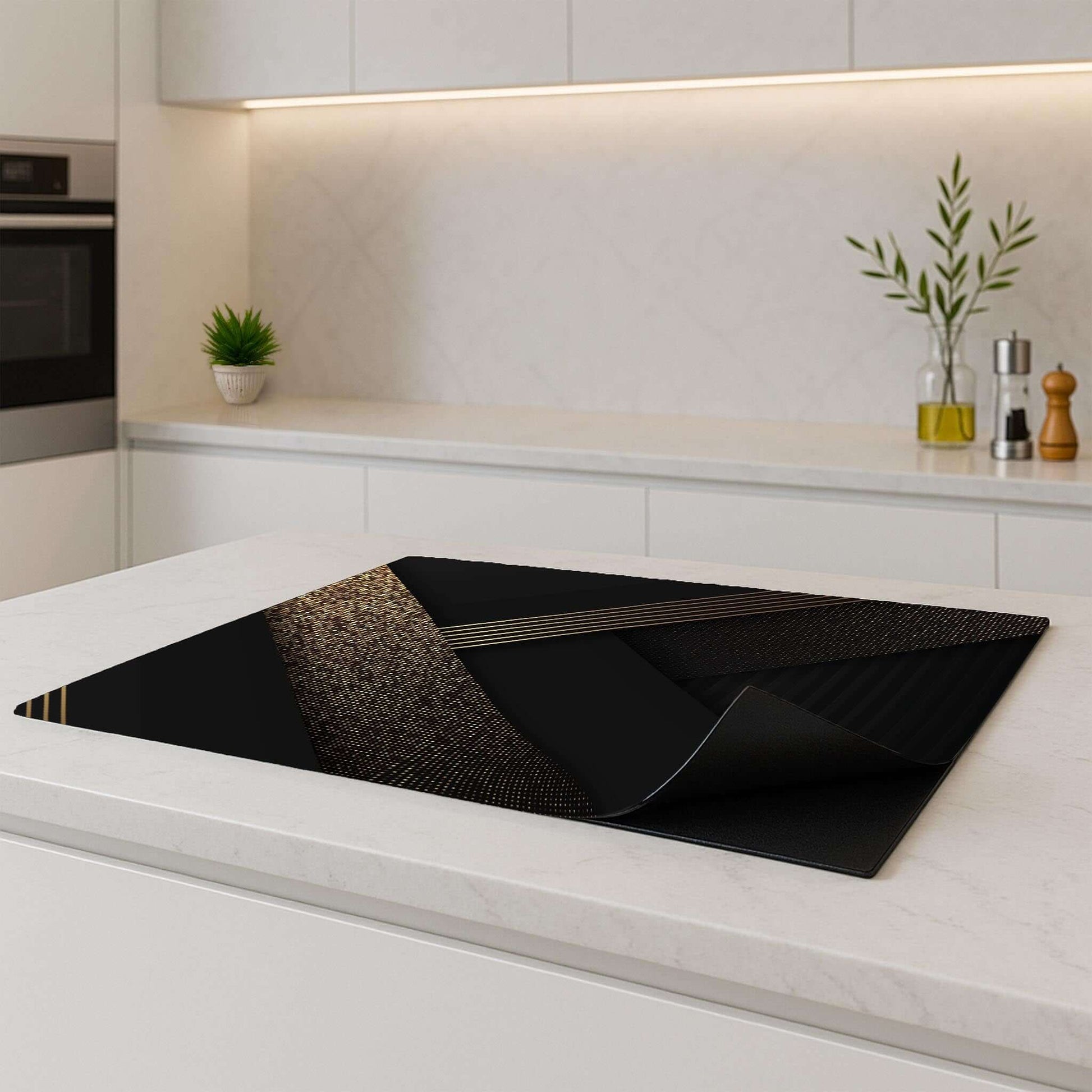 Golden Geometry inductie beschermer – zwart-goud design met opgerolde hoek op een licht keukenblad
