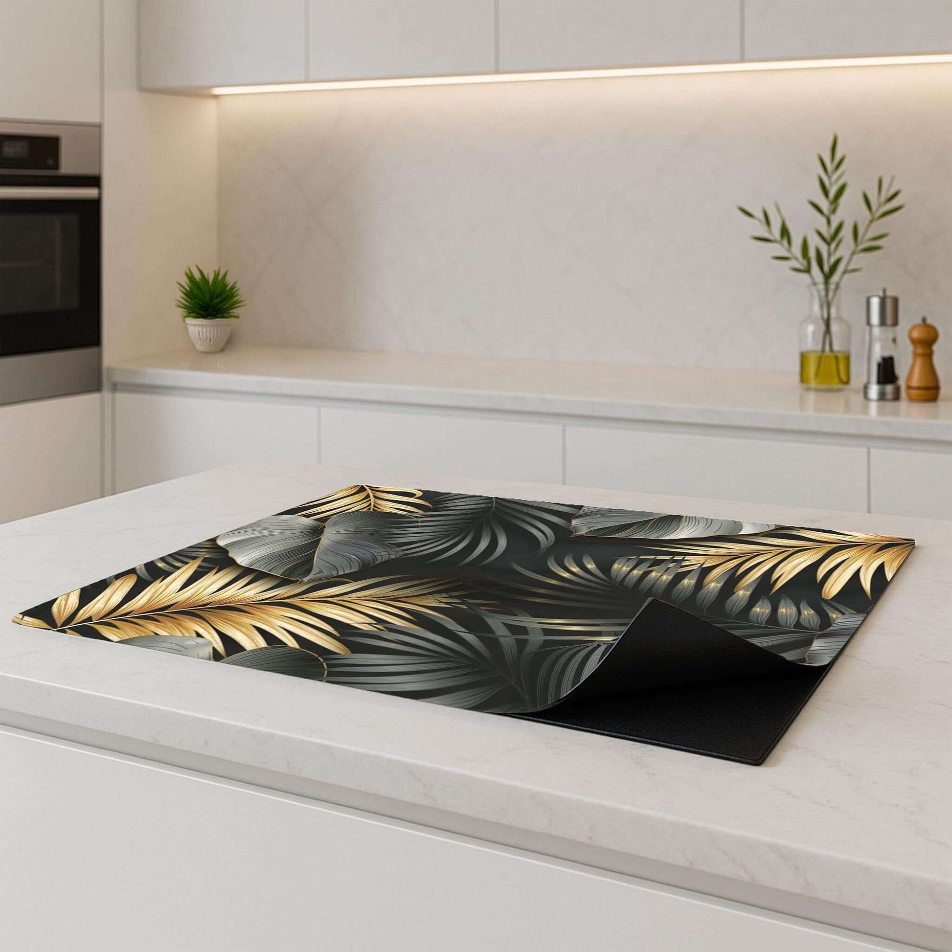 Golden Palms inductie beschermer – tropisch zwart-goud design, opgerold op licht keukenblad